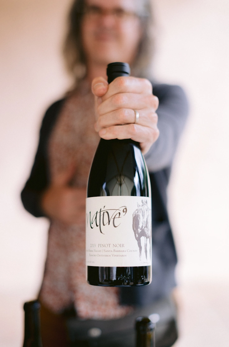 Large wine bottle in focus in foreground with Wes in the back out of focus,