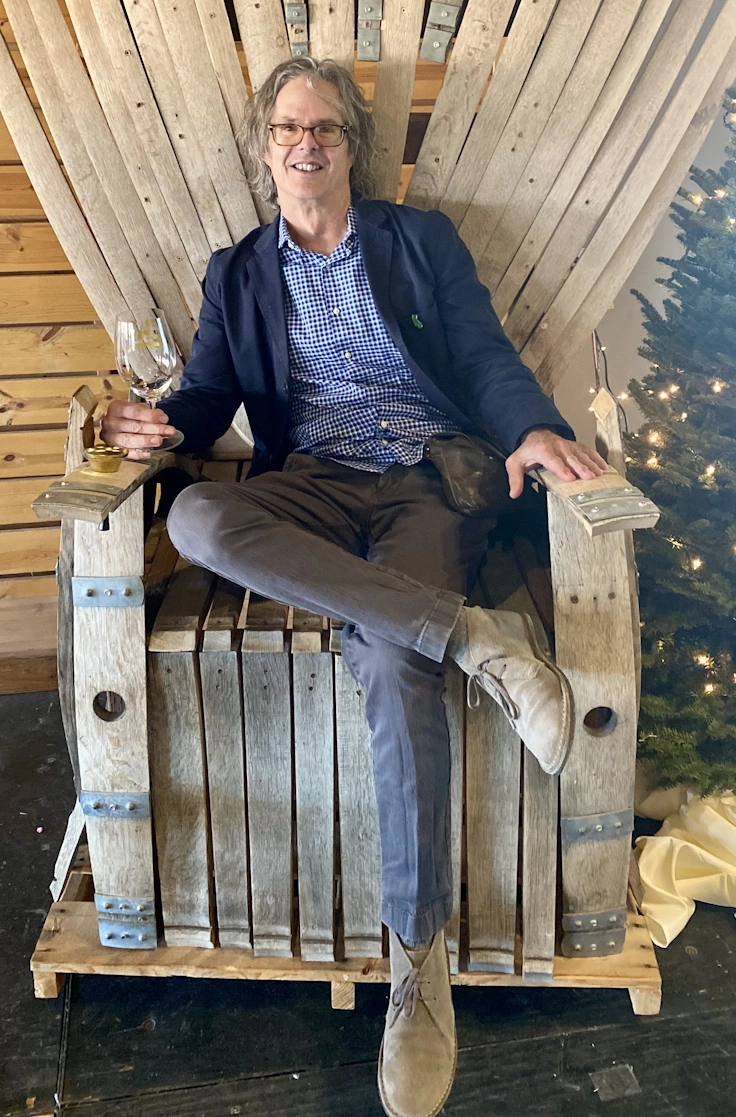 Wes Hagen, a private wine education expert, sits on a chair made of barrel staves in a blue blazer.